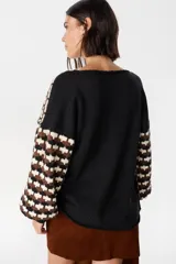 Sweater de punto con diseño geométrico de ondas en colores negro, marrón y crema. Presenta cuello redondo, mangas largas abullonadas con puños acanalados en color negro y un corte holgado.