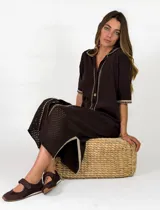 Vestido midi marrón oscuro de punto, con cuello camisero, cierre frontal de botones y mangas cortas. Presenta detalles de costuras visibles en contraste y diseño perforado en la falda.
