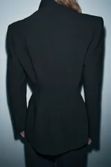Blazer entallada de Zara Woman Collection, color negro, con escote en pico, manga larga con hombreras y cierre frontal con botones ocultos. Presenta bolsillos con solapa en el delantero y detalle de nervios marcados.