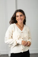 Saco de punto color blanco con cuello en V, cierre frontal con botones y apliques de flores bordadas en relieve. Presenta diseño de ochos y mangas largas con puños acanalados.