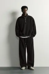 Pantalón jogger de corte relajado en color negro, confeccionado en tejido con elasticidad. Presenta cintura elástica con cordón ajustable y bolsillos laterales decorados con tachas metálicas.