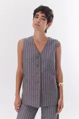 Chaleco largo color blanco con rayas verticales finas color beige, con cuello en V y cierre frontal con botones marrones. Incluye pañuelo al cuello con estampado de lunares y rayas.