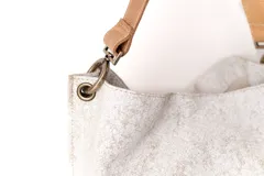 Bolso tipo hobo de cuero con acabado texturizado en tono beige claro, con correa de hombro en cuero liso color suela y herrajes metálicos en bronce envejecido.