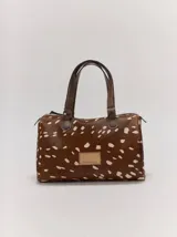 Cartera tipo baulito de cuero color marrón con estampado animal print tipo dálmata en tonos blanco y marrón, doble asa de mano y cierre superior.