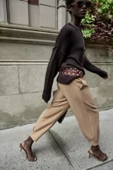 Pantalón de tiro medio con pinzas delanteras, bolsillos laterales y falsos bolsillos de vivo en la parte trasera. Presenta un corte holgado que se estrecha hacia el tobillo, con bajo acabado en pliegues y cierre frontal con cremallera, botón interior y gancho.