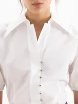 Camisa de poplín de algodón color blanco, con cuello camisero clásico, mangas abullonadas al codo con puño elástico y cierre frontal con botones.