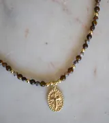 Collar de cuentas de piedra ojo de tigre y ágata, con piezas bañadas en oro y un dije ovalado con una cruz en relieve.