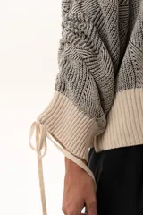 Buzo de tejido de punto con diseño geométrico en relieve, cuello redondo y mangas largas abullonadas con puños ajustables mediante lazos. Presenta un borde inferior en tejido acanalado de color crudo.