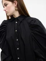 Vestido camisero blanco con botones frontales, cuello camisero, manga larga abullonada con puños ajustables y corte a la rodilla.