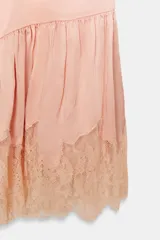Vestido corto de estilo lencero, color rosado, con escote redondo, tirantes finos ajustables, bajo acabado en volante y detalles de encaje combinado a tono.