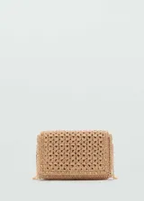 Bolso pequeño tipo bandolera confeccionado en tejido de fibra natural con diseño de espiga. Presenta detalles de tachuelas metálicas en los bordes, cierre de solapa con botón magnético y asa larga de cadena metálica dorada.