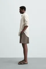 Bermuda de lino color blanco hueso, de corte relajado y tiro medio. Presenta cintura elástica ajustable con cordón, pliegues frontales y bolsillos laterales y trasero.