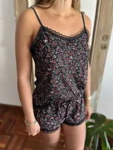 Pijama de dos piezas para mujer, compuesto por una musculosa de tirantes finos y un short a juego. Ambas prendas están confeccionadas en un tejido con estampado de pequeñas flores sobre fondo negro y cuentan con terminaciones de encaje en el escote y el ruedo.
