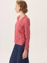 Remera de manga larga color rosado con cuello en V. Presenta detalles de costuras verticales tipo alforzas en el frente y hombros ligeramente fruncidos.