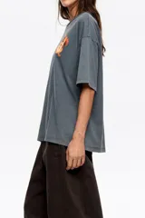 Remera de corte oversize color gris oscuro con efecto lavado, cuello redondo y manga corta amplia. Presenta un estampado pequeño de un perro salchicha con el logo de la marca en el pecho.