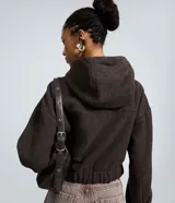 Campera tipo bomber color marrón oscuro, con capucha, cierre frontal de cremallera, bolsillos delanteros con solapa y puños elásticos.
