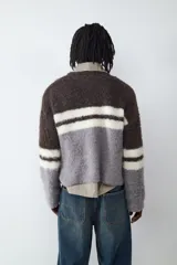 Sweater de cuello redondo con diseño de bloques de color en tonos marrón, gris y blanco, con textura de tejido de punto esponjoso y mangas largas.