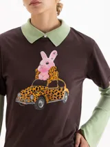 Remera de algodón pima color marrón, con estampa frontal de un conejo rosa sobre un auto con diseño de leopardo. Presenta cuello redondo y mangas cortas.