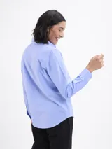 Camisa de corte clásico en tejido oxford color azul, con cuello camisero, cierre frontal de botones, manga larga con puños abotonados y un bolsillo frontal en el pecho.