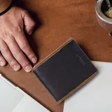 Billetera de cuero vacuno en color negro con detalles de costura y bordes en tono marrón. Cuenta con un diseño clásico, interior con doble compartimento para billetes, visor para documentos, múltiples tarjeteros y bolsillos adicionales.