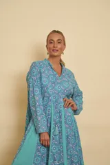 Vestido largo de algodón con estampado de mandalas en tonos celestes y azules, combinado con gajos laterales lisos en color turquesa. Presenta cuello mao con escote en V, mangas largas y silueta amplia y fluida.