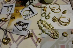 Collar con dije colgante de forma orgánica e irregular, acabado dorado, suspendido de un cordón negro de algodón natural.