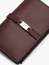 Billetera bifold Tommy Hilfiger de color bordó, confeccionada en poliuretano con acabado texturizado. Presenta un cierre principal con cremallera y un detalle frontal con logo metálico distintivo de la marca y broche.