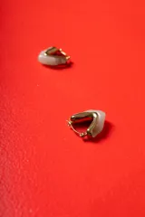 Aros tipo argolla de diseño escultórico y asimétrico, combinando metal dorado con resina en tono marmolado claro.
