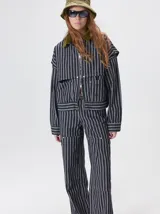 Campera de denim a rayas verticales con cuello de pana en color bordó. Presenta cierre frontal, mangas desmontables con cierre en los hombros, canesú en el pecho y bolsillos de parche cuadrados.