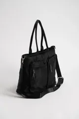 Bolso grande de estilo utilitario en color negro, confeccionado en material sintético resistente. Cuenta con doble asa de mano, correa ajustable y extraíble para el hombro, y dos bolsillos frontales con cierre y tiradores de cordón.