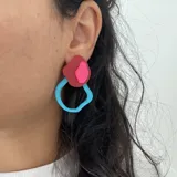 Par de aros colgantes con forma orgánica, compuestos por una estructura de acrílico celeste y una pieza superpuesta de acrílico rojo con detalle rosa.