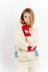 Buzo de lana merino color crema con diseño tejido de un cowboy montando un caballo en la espalda. Presenta detalles en color rojo en el cuello y en los puños de las mangas.