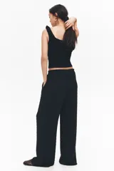 Pantalón negro de corte holgado y tiro alto, confeccionado en tejido plumeti (textura con pequeños puntos en relieve). Presenta cintura elástica fruncida con volados y cordón ajustable, además de bolsillos discretos en las costuras laterales.