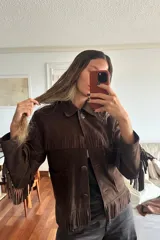 Campera de gamuza color chocolate con diseño de flecos en el pecho, espalda y mangas. Presenta cuello clásico, cierre frontal con botones y bolsillos laterales.