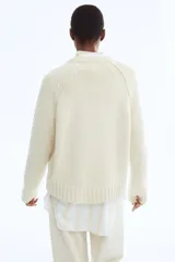 Buzo de punto con cuello redondo, manga larga raglán y detalles de costuras visibles. Presenta terminaciones acanaladas en cuello, puños y ruedo.