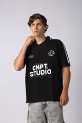 Remera tipo chomba de tejido de punto color negro, con cuello polo en V, mangas cortas y diseño holgado. Presenta detalles de rayas blancas en los hombros y estampados gráficos en color blanco en el frente.