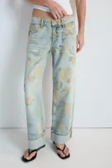 Jeans de tiro bajo confeccionados en denim, con diseño holgado y estampado integral de rosas en tonos amarillos y verdes sobre fondo celeste claro. Cuenta con cinco bolsillos, trabillas para cinto y botamangas con vuelta.