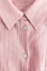 Camisa entallada de mezcla de viscosa en color rosado, con efecto arrugado y bajo levemente acampanado. Presenta cuello camisero, cierre frontal de botones, canesú en la espalda y pliegues en la cintura que definen la silueta. Cuenta con mangas largas y puños abotonados.