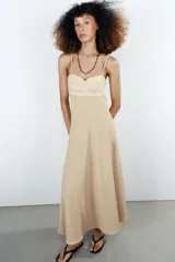 Vestido midi de color beige con escote recto adornado con un panel de encaje semitransparente, tirantes finos ajustables y falda fluida con cierre lateral con cremallera oculta.