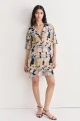 Vestido camisero corto con estampado abstracto en tonos beige, azul, negro y amarillo. Confeccionado en lino y seda, con cuello camisero, mangas cortas y cierre frontal con botones.