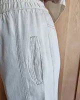 Pantalón de algodón color arena, de corte recto y holgado, con cintura elástica y detalle de costuras horizontales decorativas en la parte inferior de las piernas.