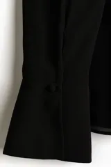 Blusa oversized negra de tejido transparente, con cuello fular, escote profundo y mangas largas con puños anchos.
