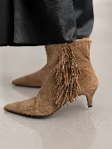 Bota de caña corta en cuero gamuzado color marrón, con diseño de punta fina y taco fino de 5 cm. Presenta un detalle de flecos laterales que aportan movimiento y estilo.