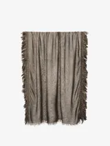 Pañuelo fino de tejido ligero, color gris, con flecos largos y densos en los bordes laterales y flecos más cortos en los bordes superiores e inferiores.