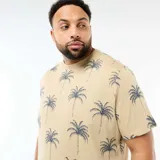 Remera de manga corta y cuello redondo en color beige con estampado integral de palmeras en tono azul oscuro.