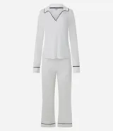Pijama de dos piezas confeccionado en tejido ribana, compuesto por una blusa de manga larga con escote en V y cuello tipo polo, y un pantalón de corte recto. Ambas prendas presentan un diseño liso en color blanco con detalles de biés en contraste color negro en el cuello, puños y ruedo.