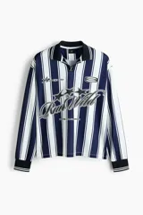 Camiseta de fútbol de manga larga confeccionada en malla estampada, con diseño de rayas verticales en azul marino y blanco. Presenta cuello polo negro con ribete blanco, cierre frontal parcial en V, y puños elásticos negros con líneas blancas. Cuenta con estampado frontal con gráficos de estrellas y la inscripción "Run Wild".