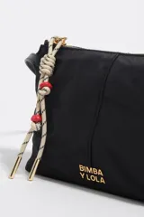 Bolso bandolera mini de Bimba y Lola en color negro, con cierre de cremallera superior, asas cortas de mano y tirador decorativo de cuerda con cuentas rojas. Presenta el logotipo de la marca impreso en letras doradas en la parte frontal.