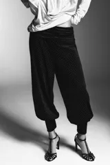 Pantalón negro de tiro bajo, confeccionado en terciopelo con pequeños puntos brillantes. Presenta cintura elástica con pliegues, caída ancha tipo baggy y puños ajustados en los tobillos.