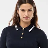 Sweater de punto acanalado en color azul marino, con cuello polo, manga corta y cierre frontal con botones dorados. Presenta detalles de rayas blancas en el cuello, los puños y el ruedo.